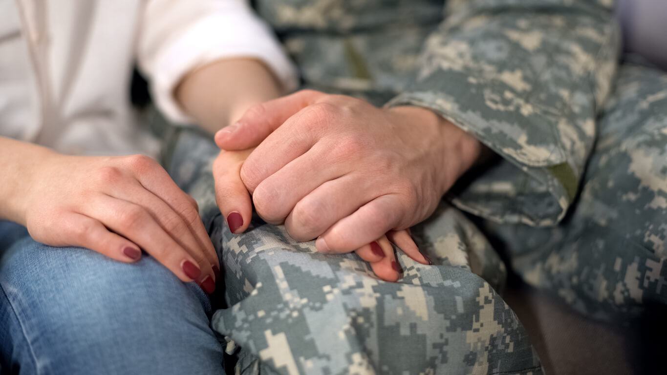 Military couple holding hands, contemplating divorce