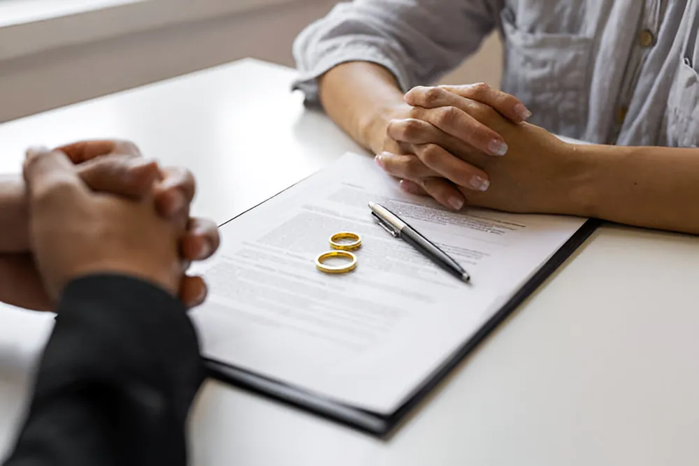Couple reviewing and signing a divorce settlement agreement with wedding rings on legal documents during a consultation.