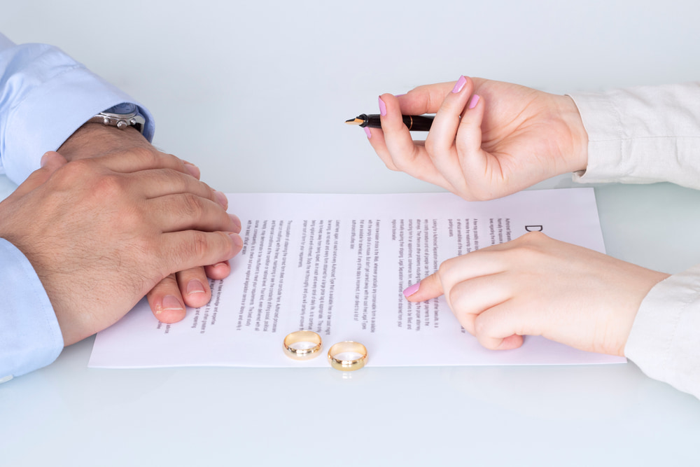 Two people reviewing and signing family law documents with wedding rings and a pen on the table during a legal consultation.